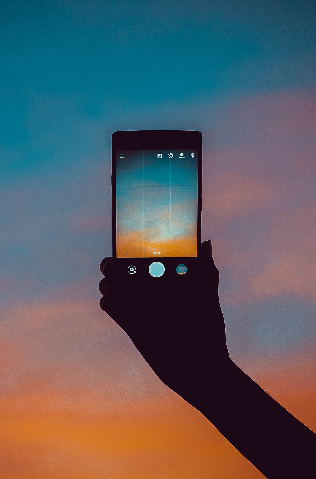 Main tenant un téléphone qui photographie un ciel au coucher du soleil