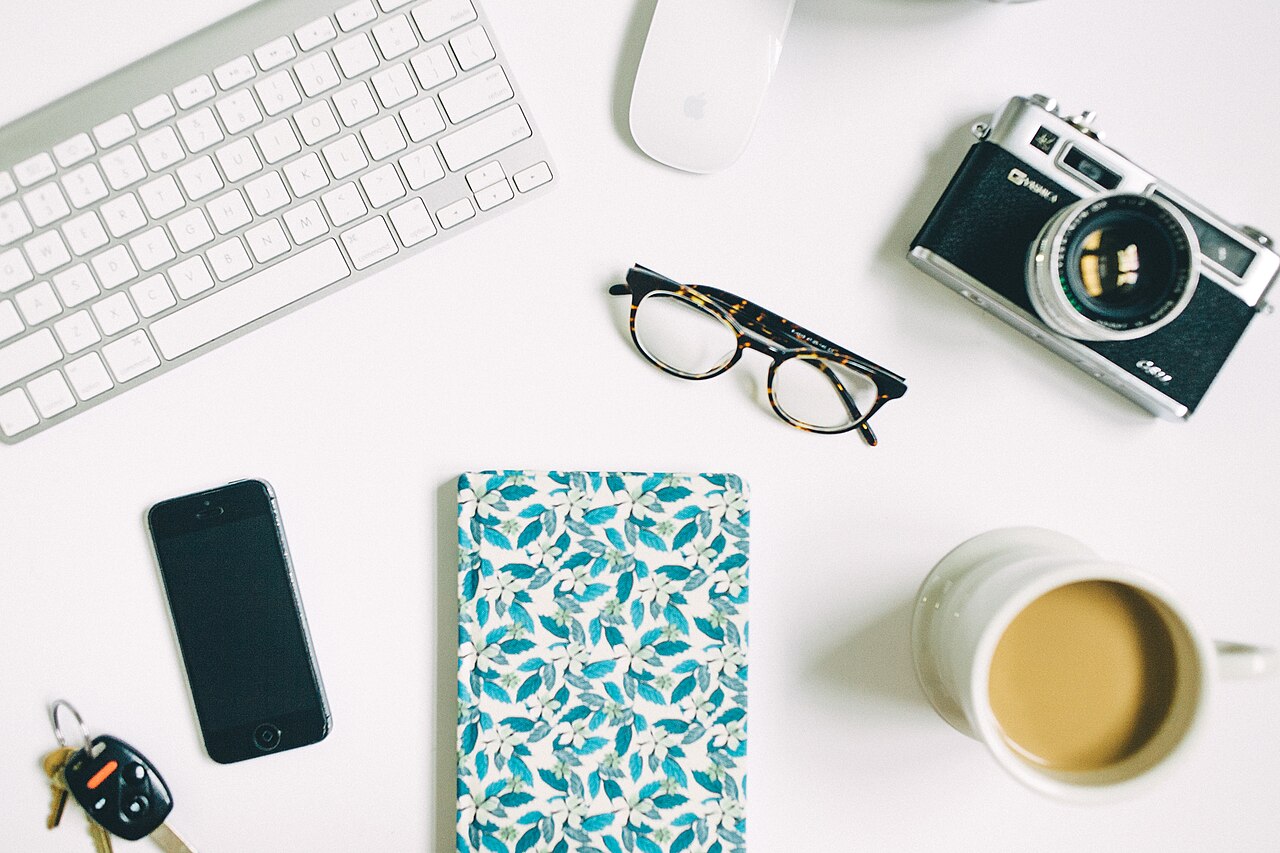 Bureau vu de dessus : clavier, carnet, appareil photo, téléphone et tasse de café